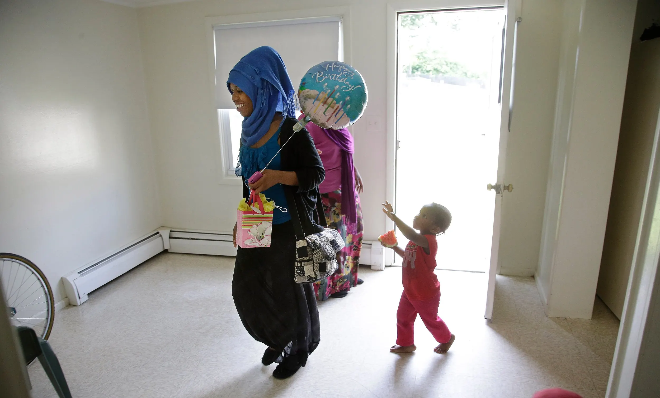 Somali Refugees — Saadiya Idoor, 17, walks into her family's apartment after school carrying her backpack and a birthday balloon as her youngest sister Yasmine, 2, reaches for the balloon on Tuesday, June 17, 2014, in Springfield, Massachsetts. Today is Saadiya's birthday and Yasmine had her eye on the balloon as soon as her sister walked through the door.  (AP Photo/Stephan Savoia)  © The Associated Press