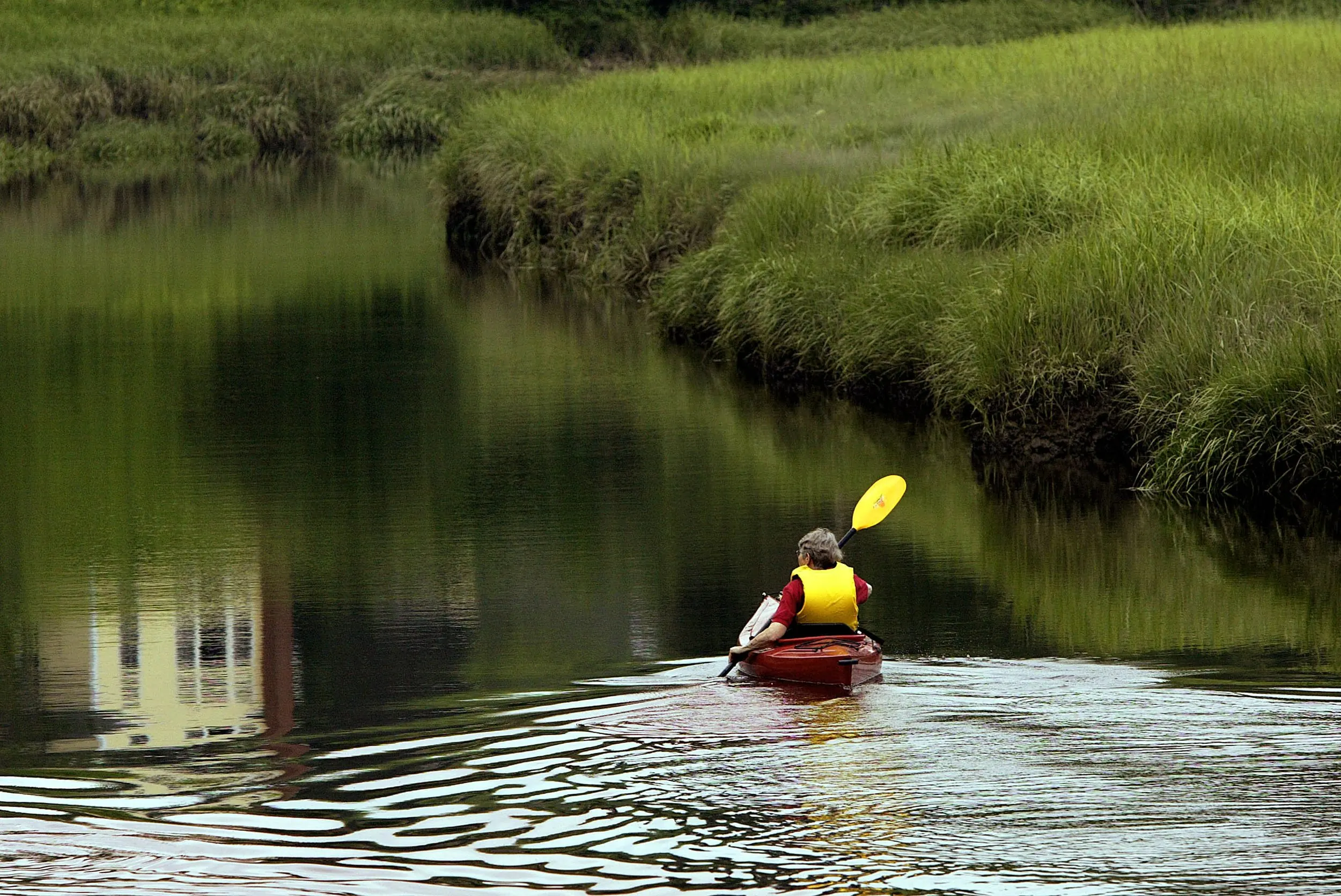 From Riding To Gliding — Kitty Bassett, a graduate of the Wellesley College class of 1950, paddles her kayak up the Kennebunk River near her home in Arundel, Maine Thursday morning, June 30, 2005. Bassett enjoys kayaking the river during the summer months, an activity she began after her children insisted she sell her motorcycle at the age of 74.  (AP Photo/Stephan Savoia)  © The Associated Press