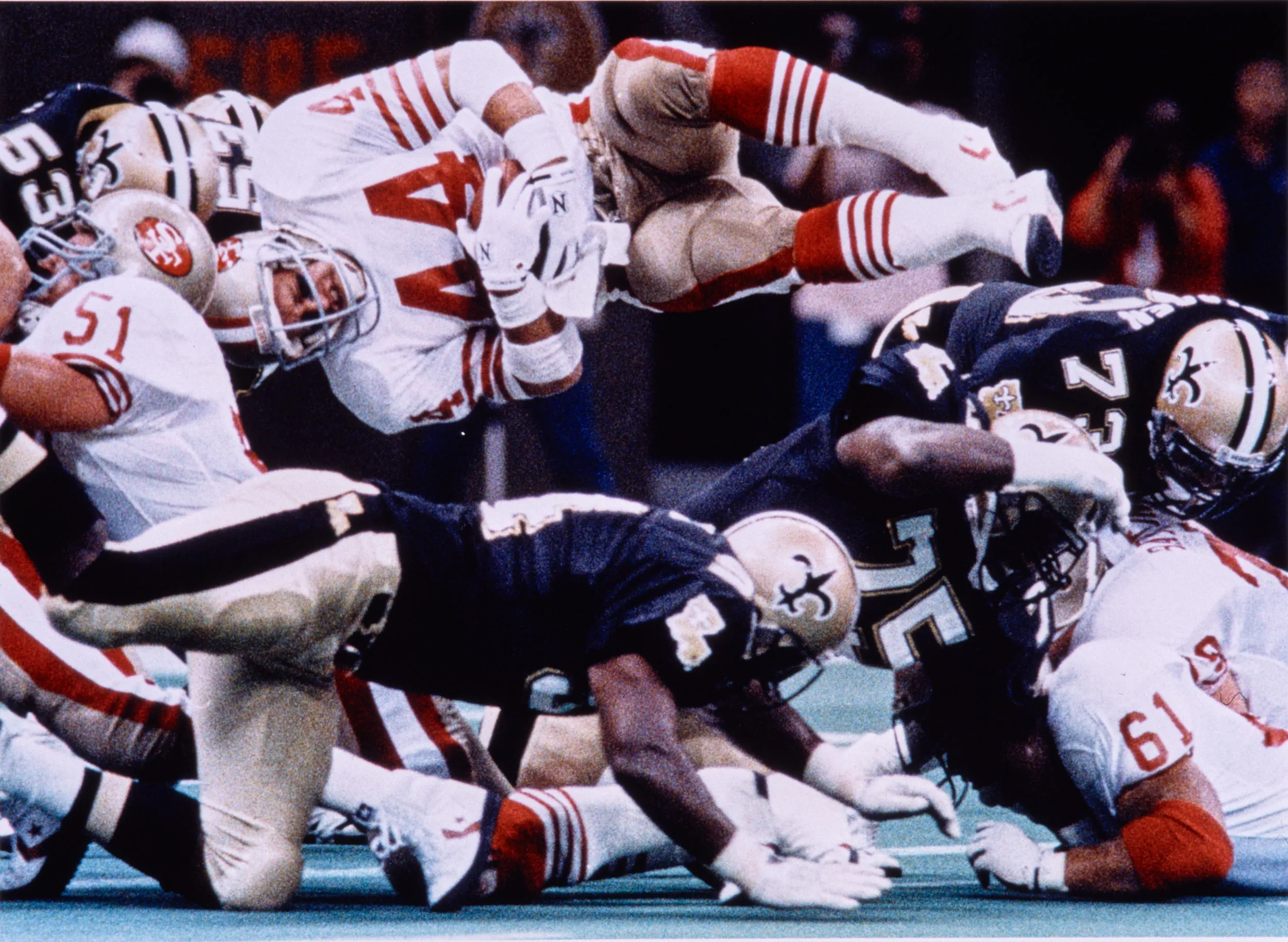 Just Short — San Francisco 49’ers fullback Tom Rathman (44) tucks the football as he leaps over the New Orleans Saints defensive line toward the end zone during an NFL football game at the Louisiana Superdome in New Orleans, Louisiana. Rathman came up inches short on the play, only to cross the goal line for a touchdown on the next play with the exact same play called. Circa Mid 1980s.  (AP Photo/Stephan Savoia)  © The Associated Press